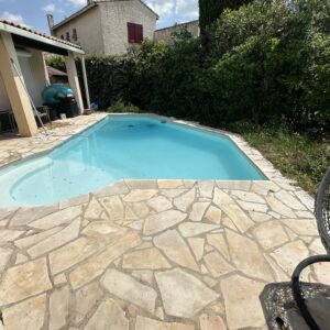 a pool with a stone patio and a house in the background